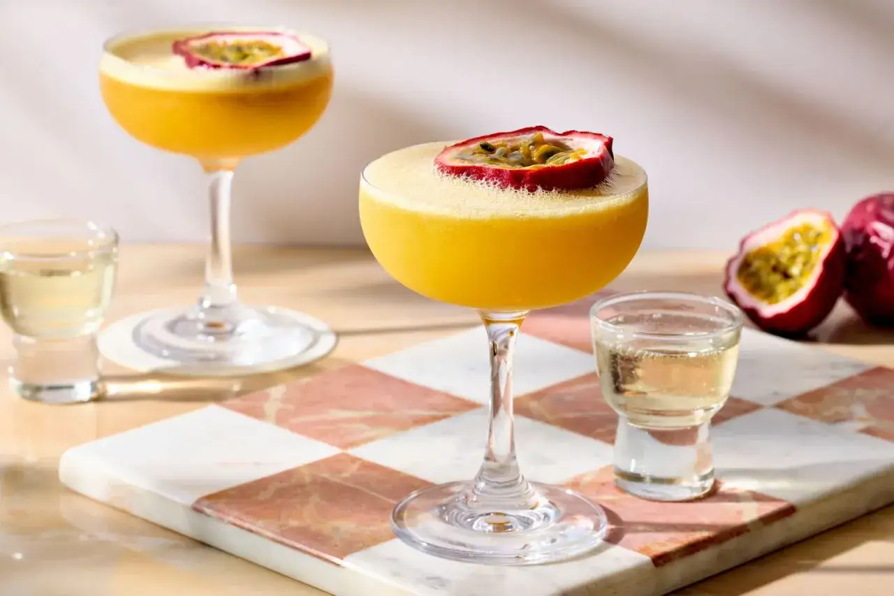 Två Pornstar Martini-drinkar med passionsfrukt, en shot och passionsfrukter på en marmorerad bricka.