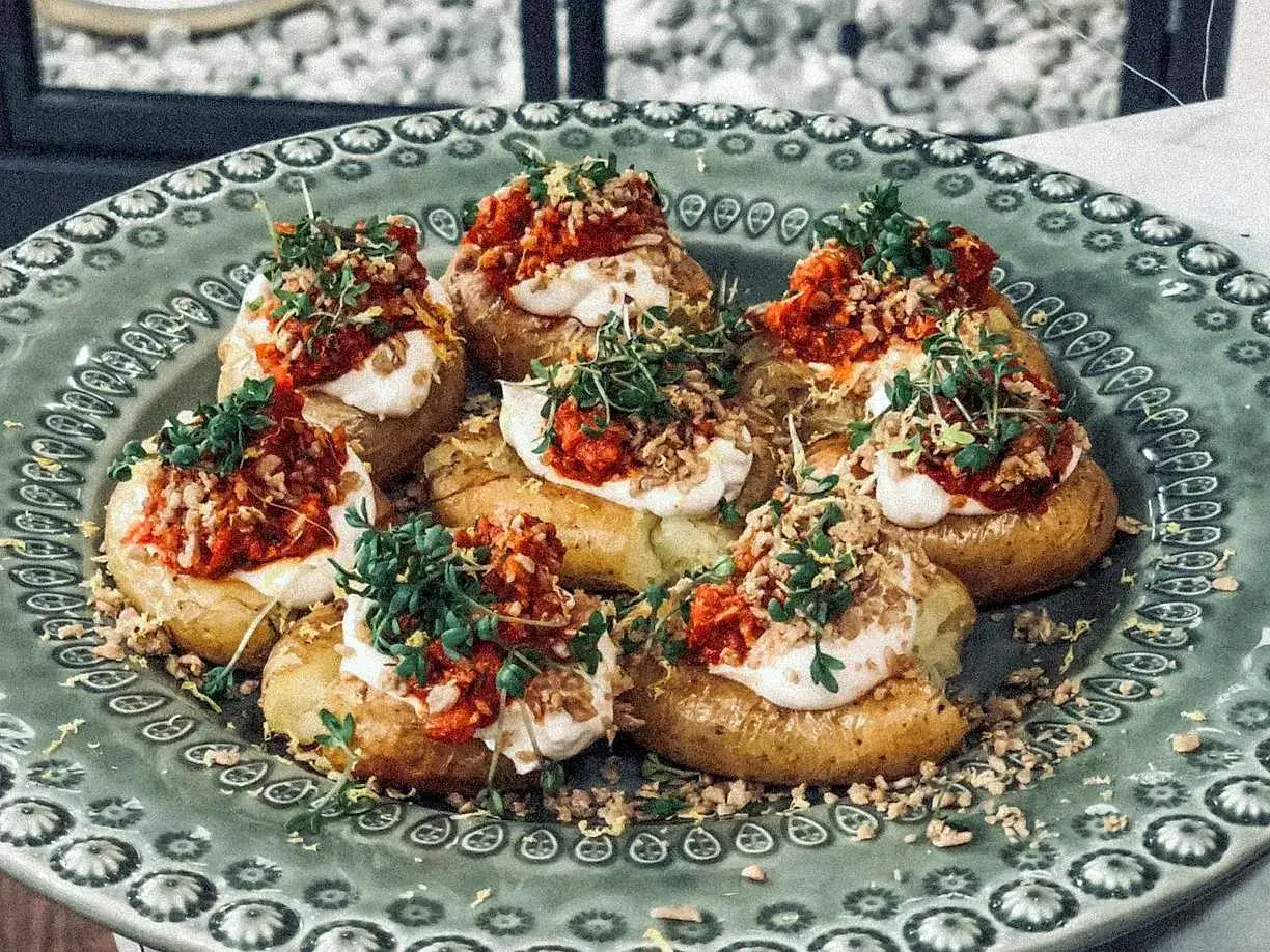 Små, bakade potatisar toppade med krämig sås, kryddig tomatsalsa och färska örter. En läcker variant av patatas bravas.