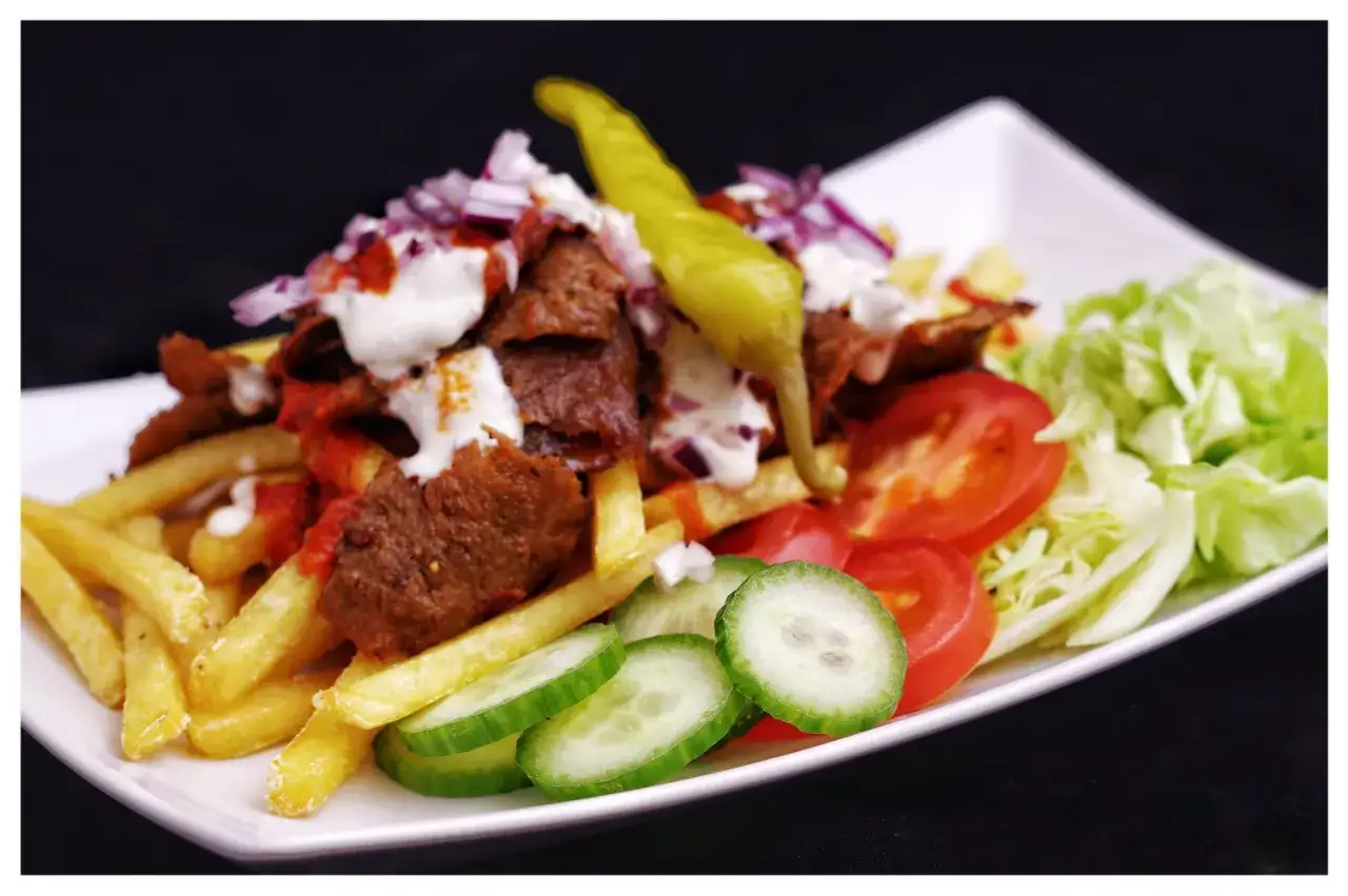 En tallrik med kebab, pommes frites, tomater, gurka, sallad och en grön chili. Perfekt för dig som söker ett gott kebabsås recept.