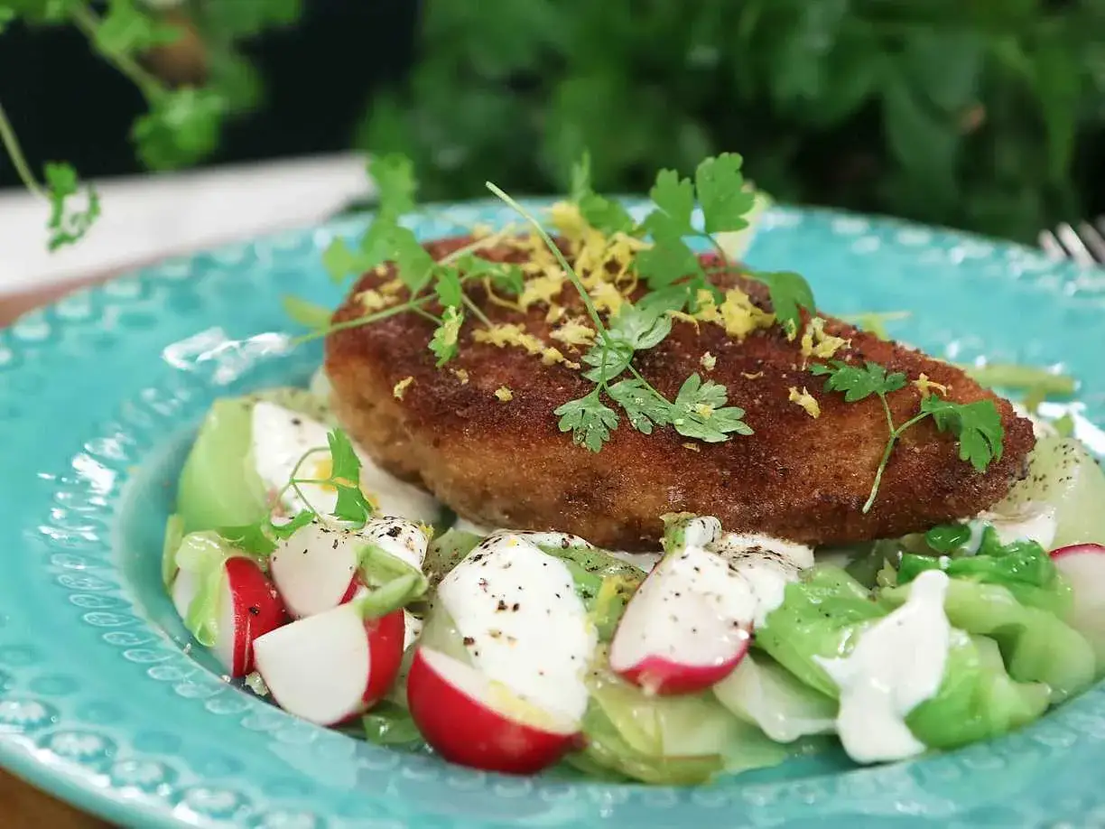 Krispig kyckling Kiev med en fräsch sallad av kål, rädisor och krutonger, toppad med citronzest och persilja.