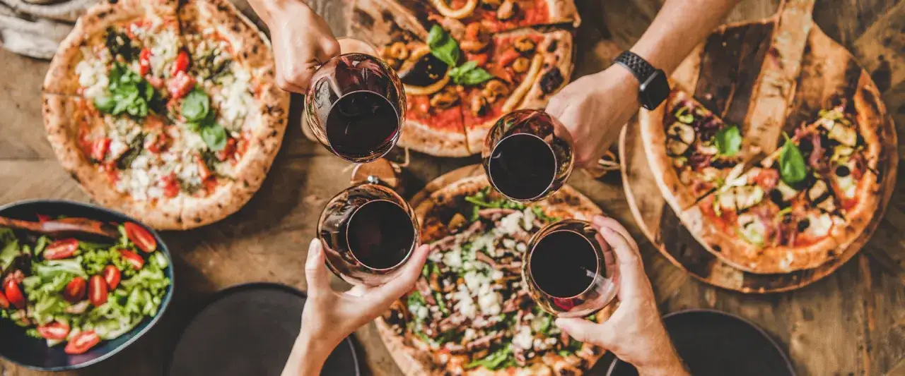 En härlig kväll med vänner, pizza och rött vin. Flera olika pizzor och en fräsch sallad dukas upp på ett rustikt träbord.