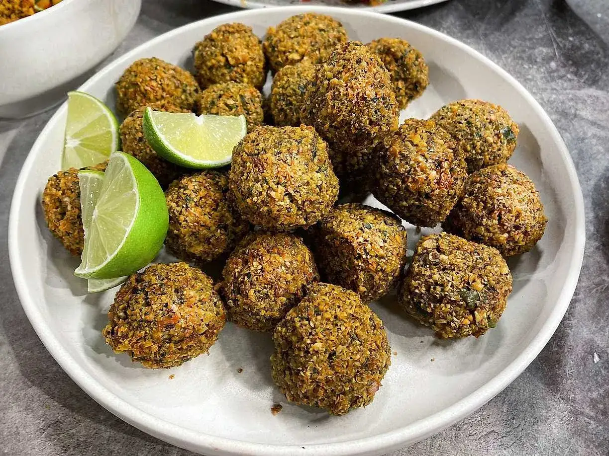 En tallrik med gyllene falafelbollar, perfekt för ett gott falafel recept. Garnerad med färska limeklyftor.