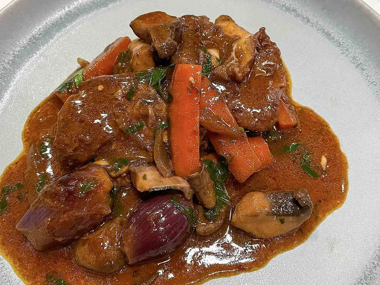 En mustig gryta med mört kött, morötter, champinjoner och rödlök i en rik sås. En klassisk coq au vin som ser otroligt god ut.