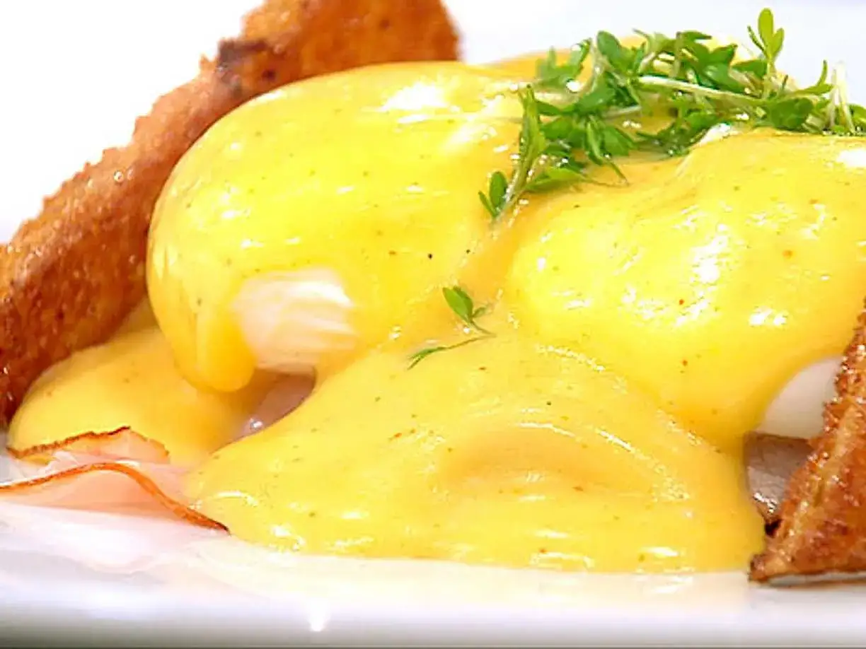 En krämig hollandaisesås täcker perfekt pocherade ägg på rostat bröd, en klassisk eggs benedict.