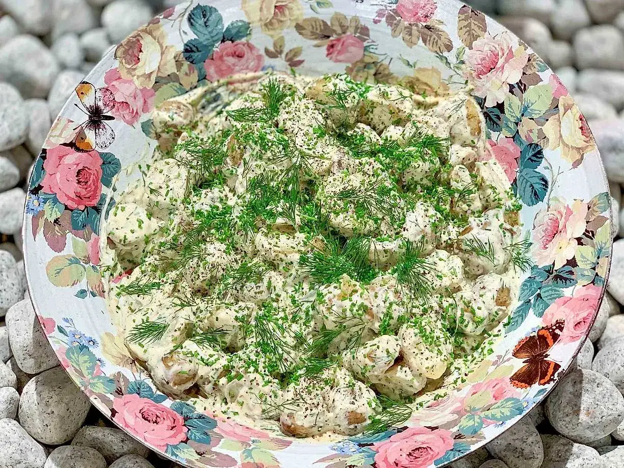 Enkel potatissallad med krämig crème fraiche, toppad med färska örter. Serveras i en vacker skål med blomstermönster.
