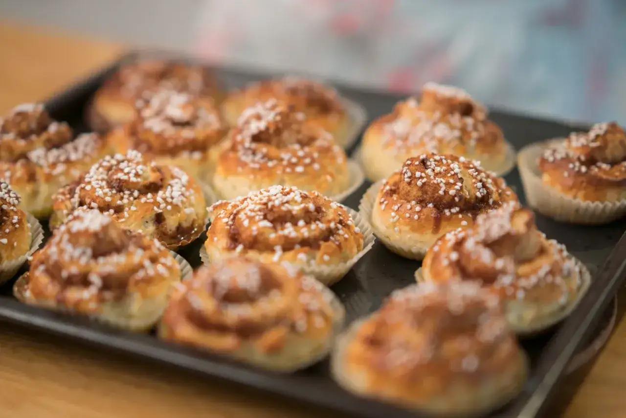 En plåt med nybakade, glutenfria kanelbullar, toppade med pärlsocker. Doften av kanel sprider sig.