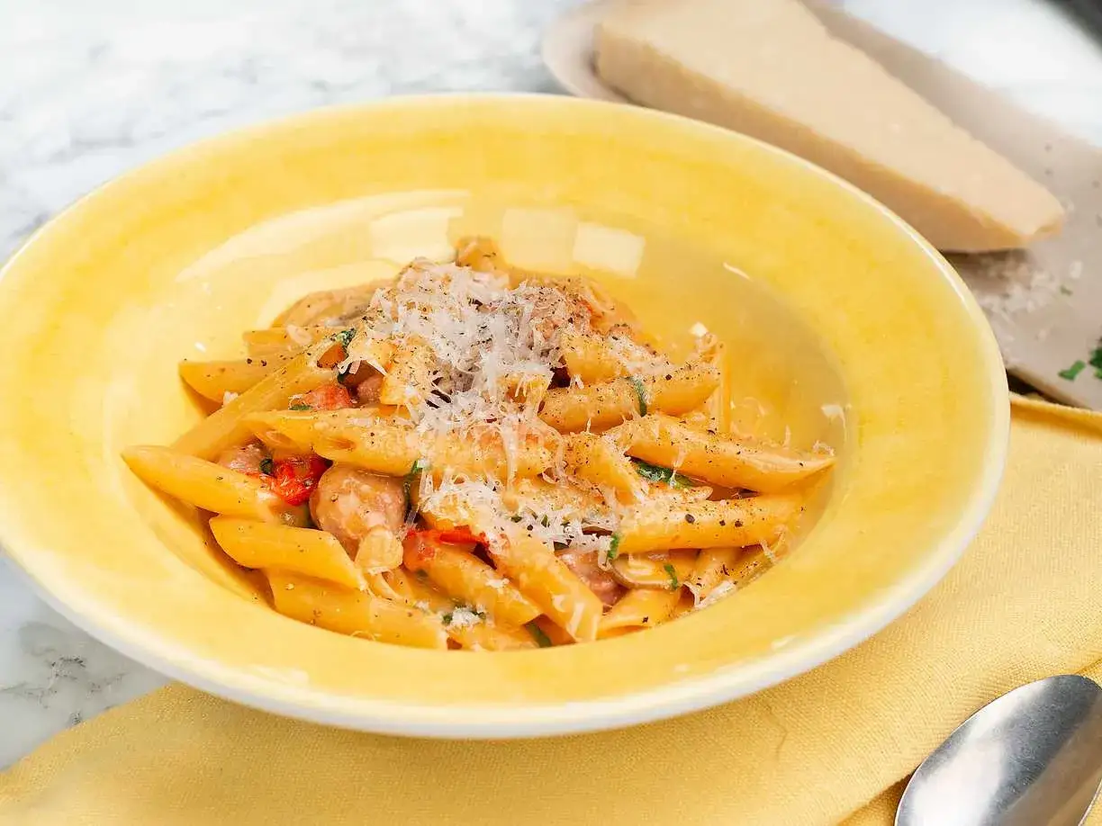 En gul skål med salsicciapasta, toppad med riven parmesan. En bit parmesan ligger bredvid.