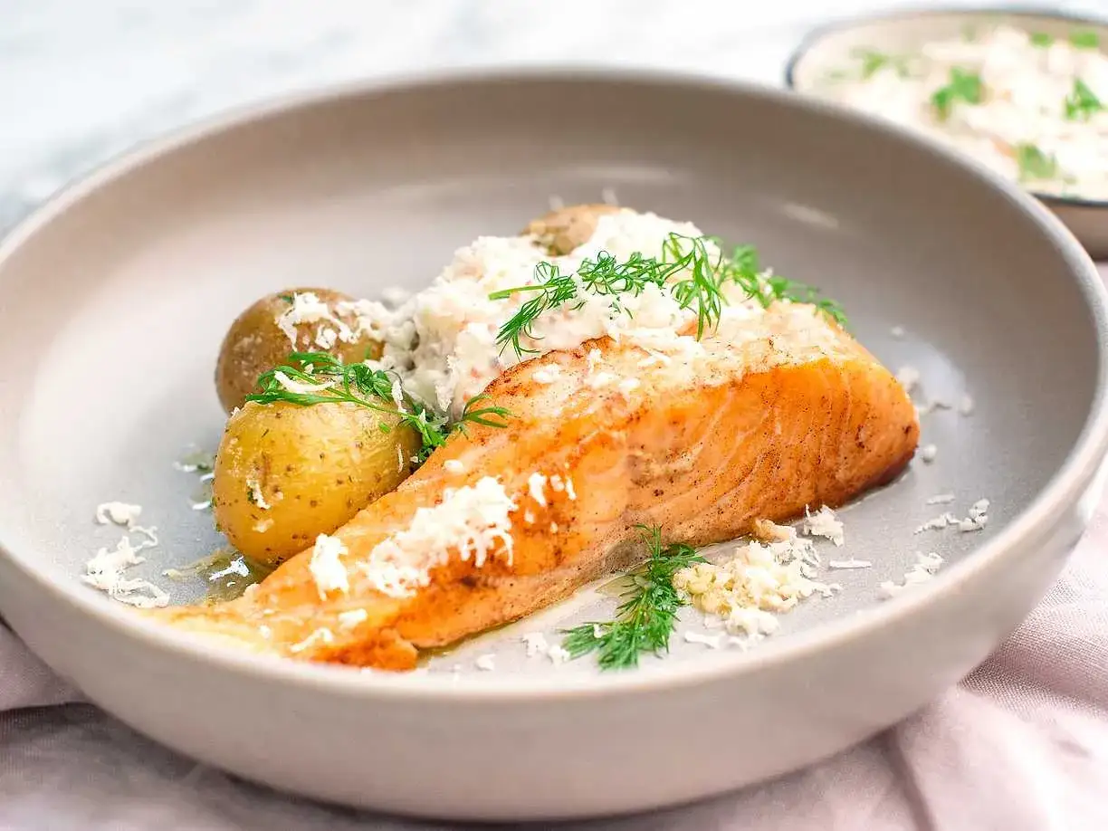 En portion stekt lax med småpotatis och en krämig sås, toppad med dill och riven ost. En klassisk svensk rätt.