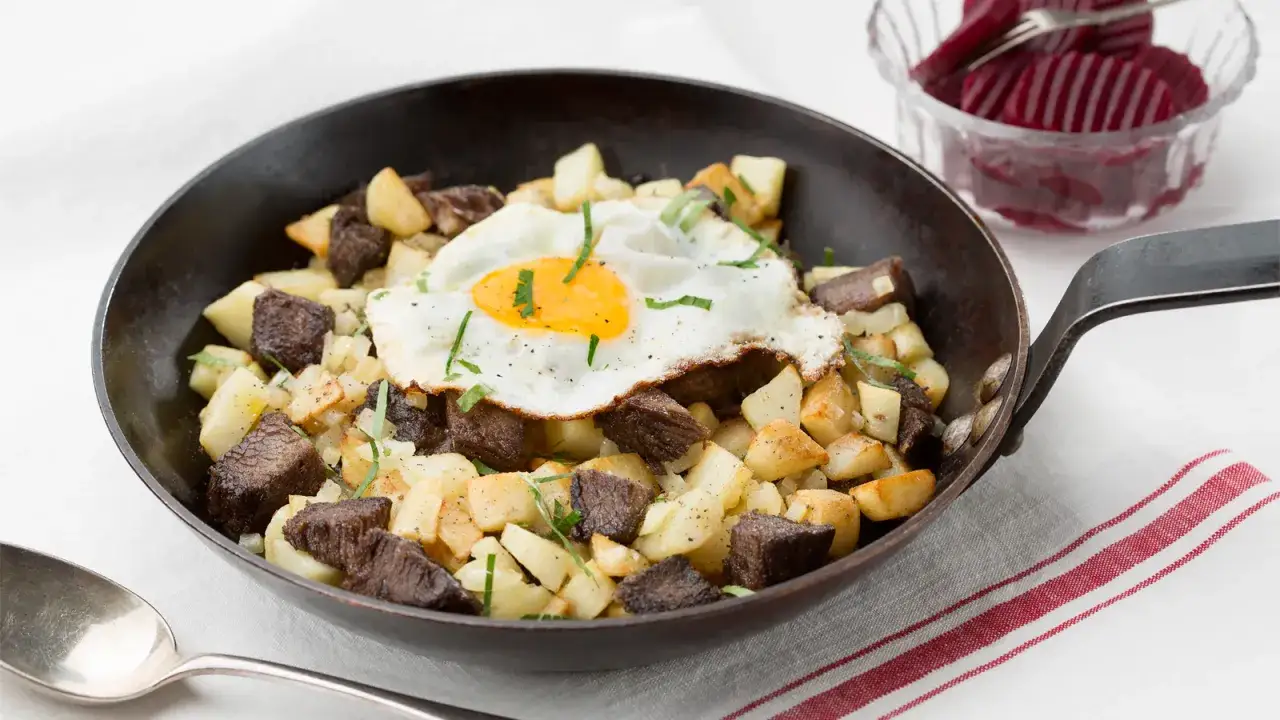 En stekpanna med pytt i panna, toppad med ett stekt ägg och garnerad med örter. Serveras med inlagda rödbetor.