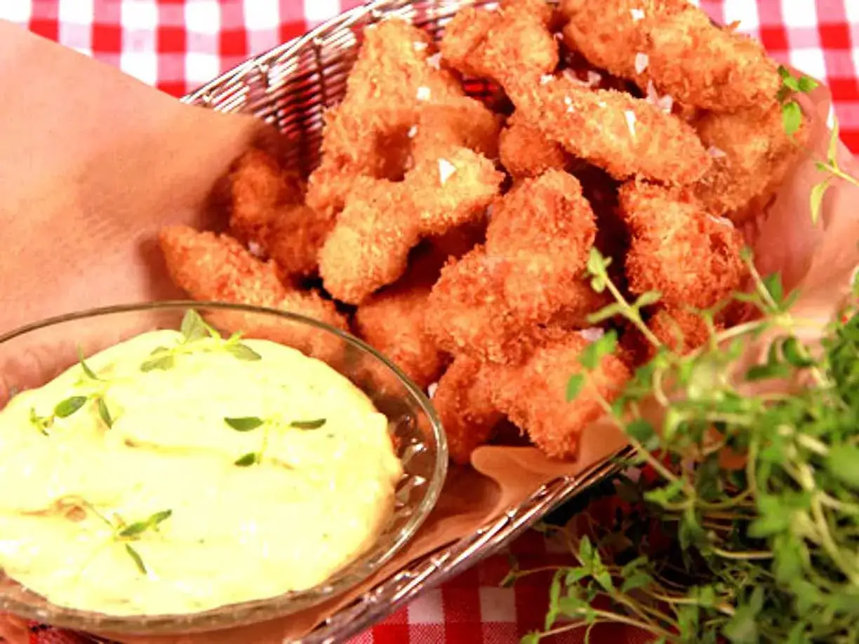 Korg med gyllene chicken nuggets, en skål med krämig dipp och färska örter.