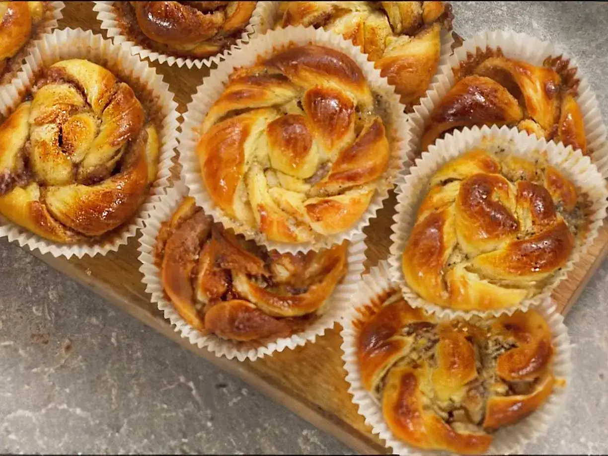 Nybakade bullar med mandelmassa, kanel och vallmofr&ouml;n i pappersformar p&aring; en tr&auml;bricka.