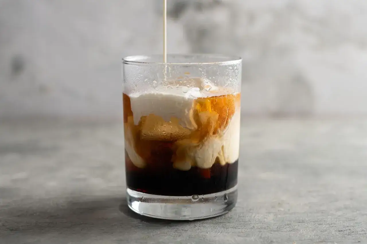 Grädde virvlar ner i en mörk vätska i ett glas, vilket skapar ett vackert mönster som påminner om en White Russian.