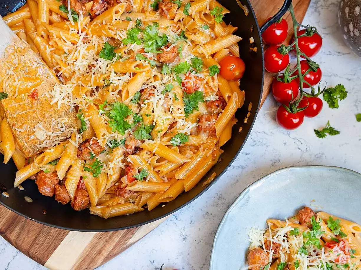 En stor panna med krämig chorizo pasta, toppad med riven ost och färsk persilja. Bredvid syns en tallrik med samma läckra rätt.