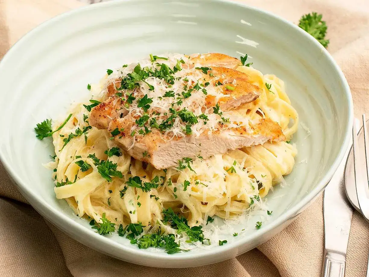 En krämig portion chicken alfredo med tagliatelle, toppad med grillad kyckling, parmesan och färsk persilja.