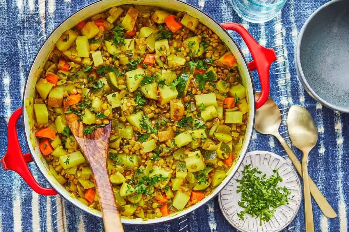 En stor gryta med mustig vegansk mat, full av linser, potatis, morötter och zucchini, toppad med färsk persilja.