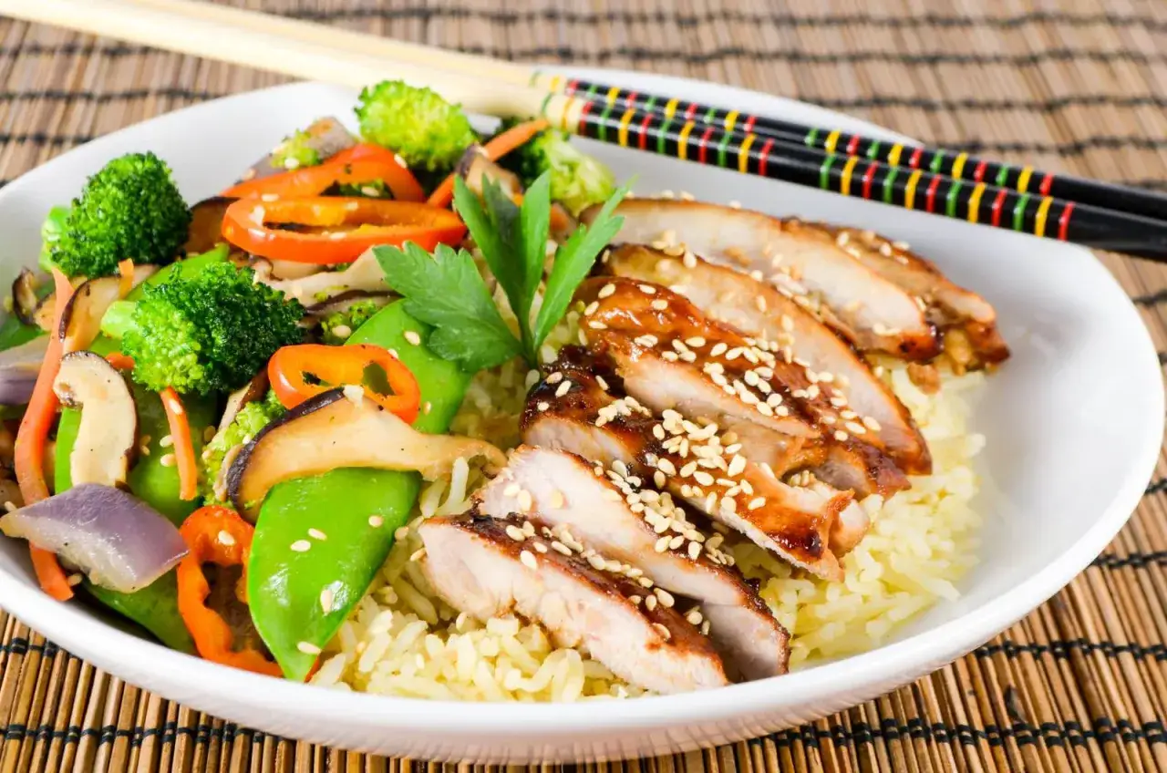 En skål med ris toppad med saftig kyckling teriyaki, wokade grönsaker och sesamfrön.