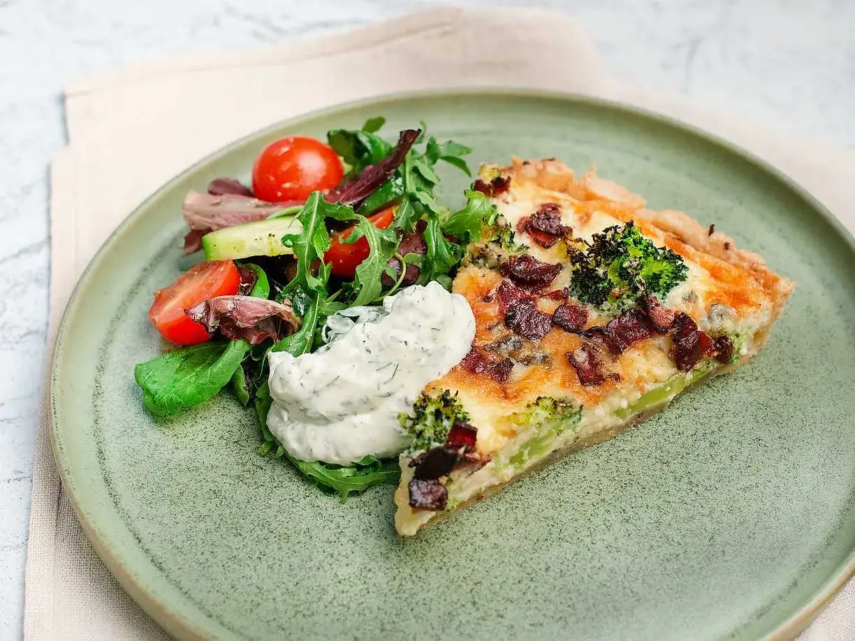 En bit ost och broccolipaj med knaperstekt bacon, serverad med en fräsch sallad och en klick örtdressing.