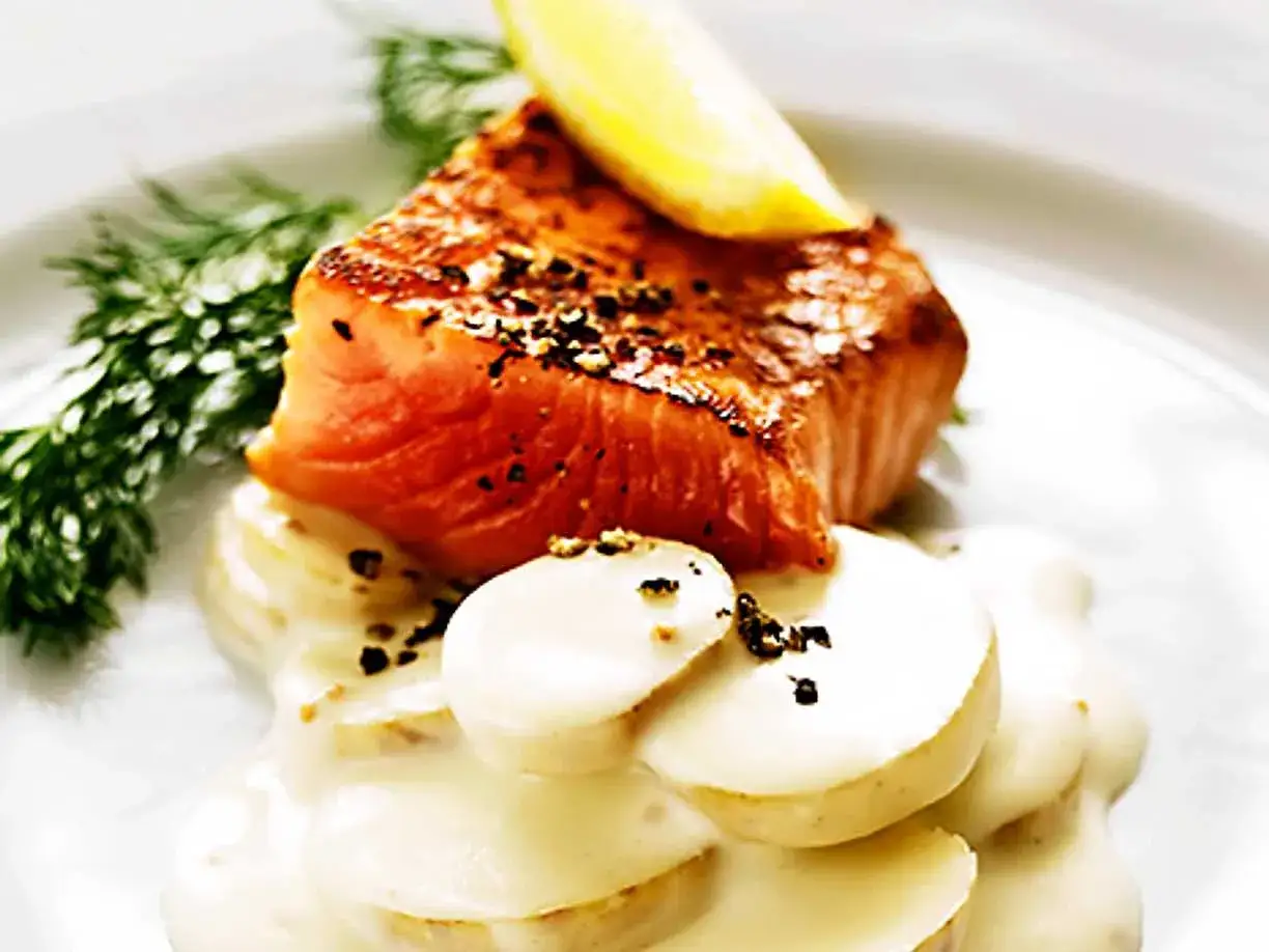 En bit stekt lax med citronskiva och dill, serverad på potatis med en krämig sås. Perfekt till ditt gravlaxsås recept.