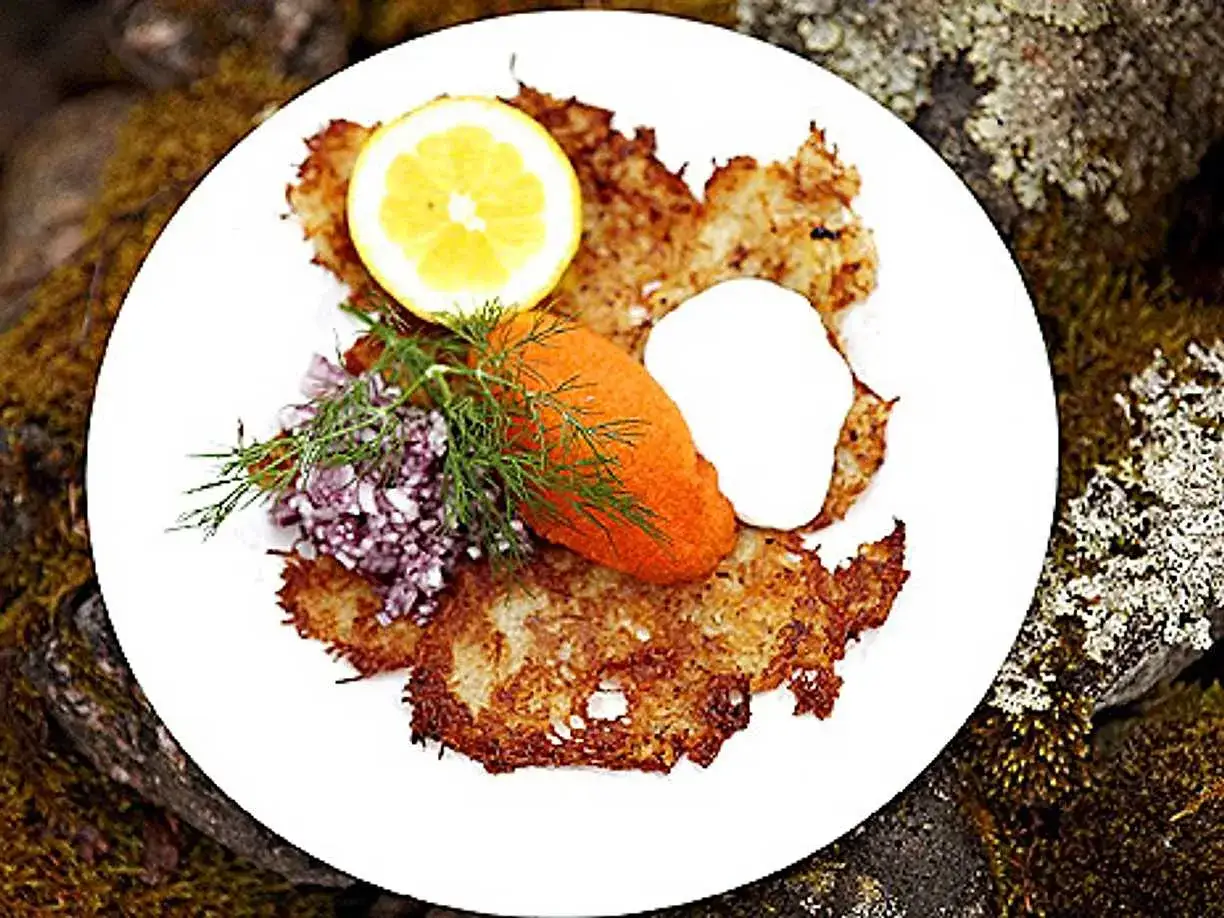 En tallrik med gyllene rårakor, toppad med rom, gräddfil, dill, rödlök och en citronskiva. Ett härligt råraka recept!