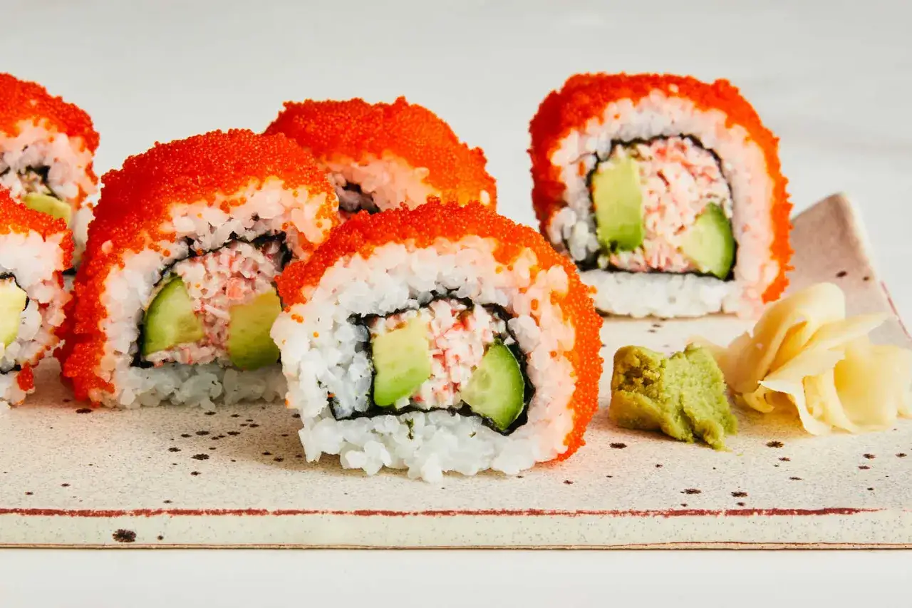 En närbild på en california roll med ris, krabba, gurka och orange rom. Serveras med wasabi och ingefära.