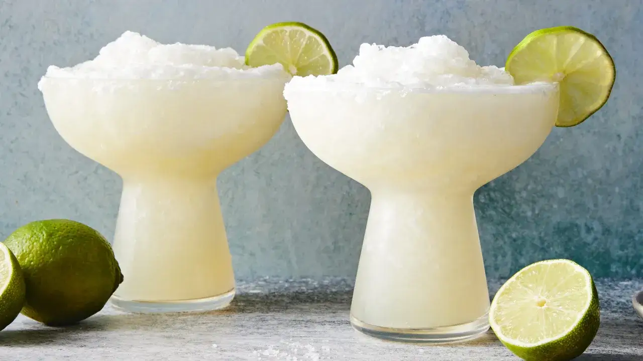 Två frostiga margaritas med lime och saltkant, redo att avnjutas. Perfekt för ett frozen margarita recept.