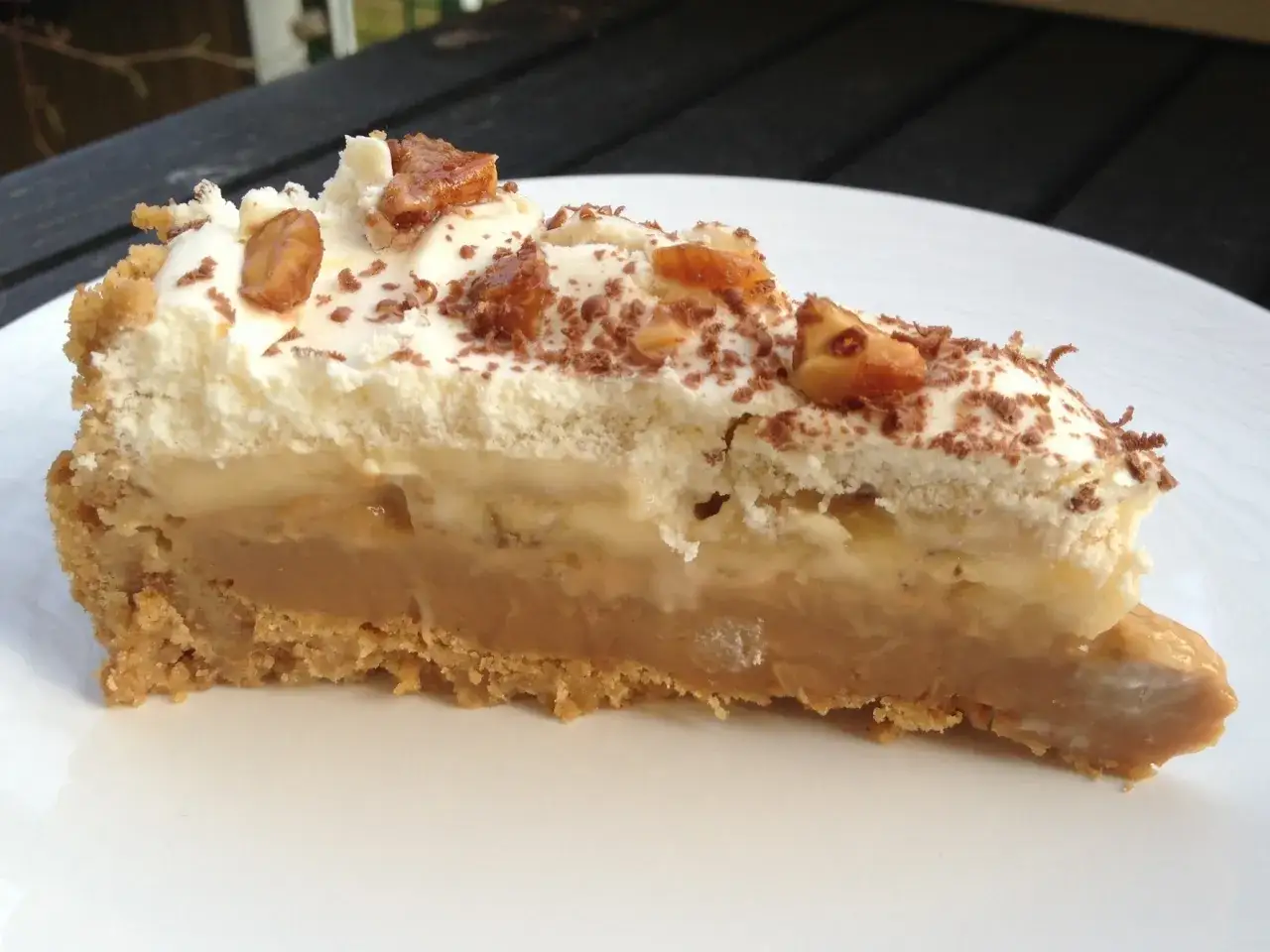 En generös bit banoffee paj med krämig kolasås, banan och vispgrädde, toppad med nötter och choklad.