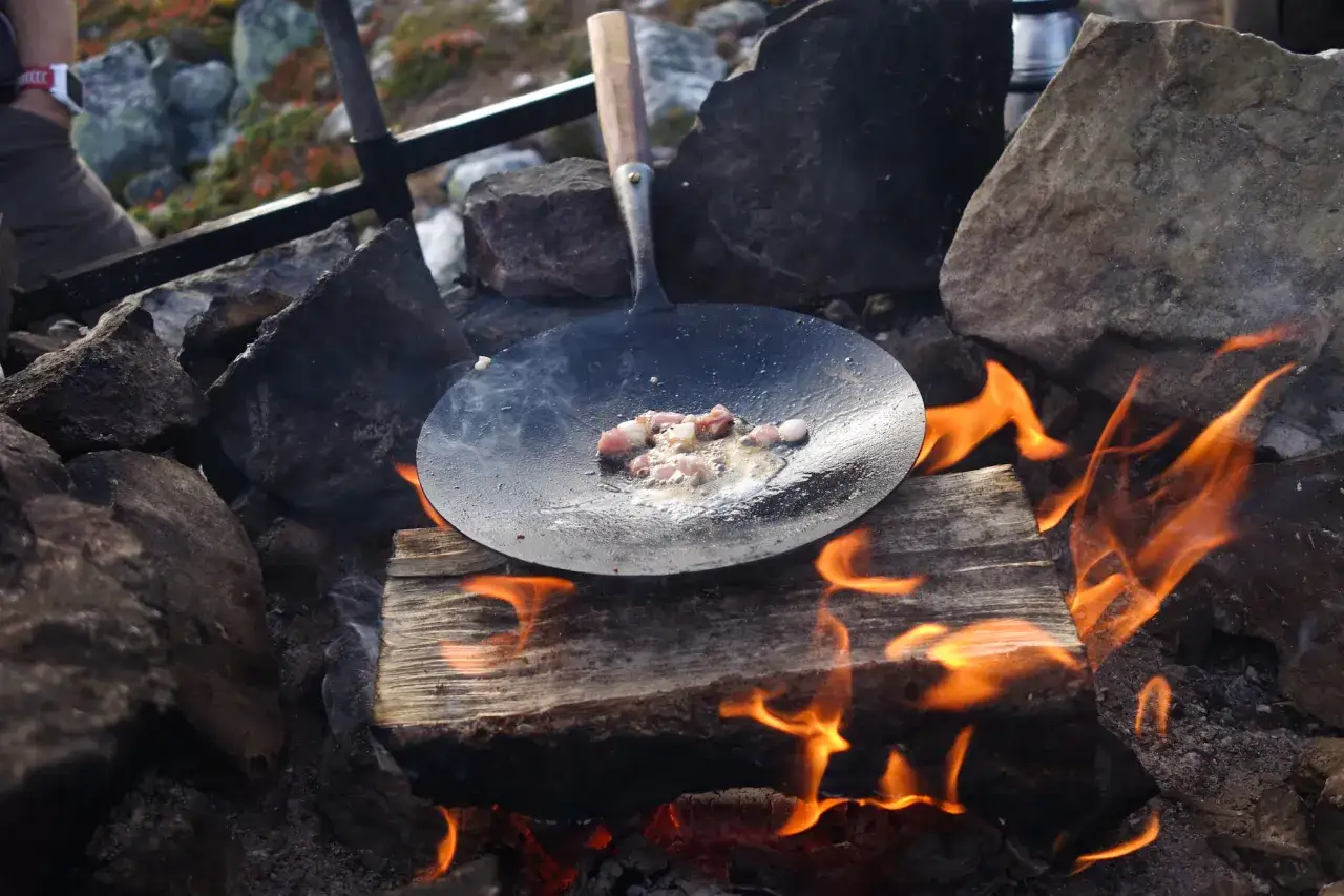 Stekt fläsk på en stekpanna över öppen eld, en del av ett kolbulle recept. Elden sprakar och röken stiger.