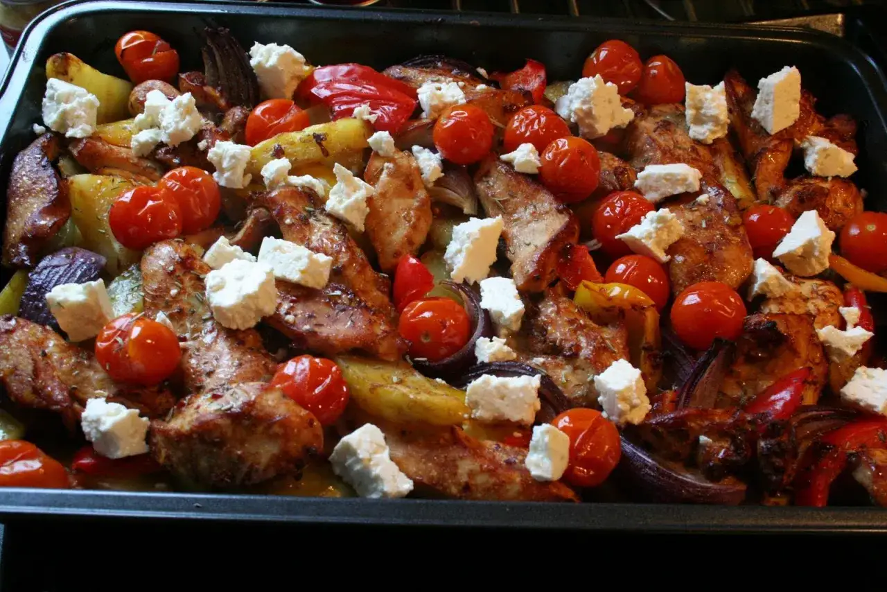 En härlig grekisk pyttipanna med kyckling, potatis, tomater, paprika och fetaost i en ugnsform.