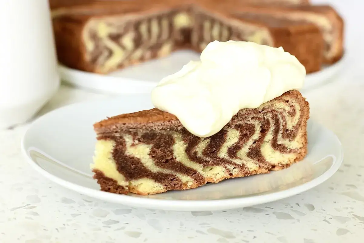 En skiva tigerkaka med härlig marmorering, toppad med grädde. Ett perfekt tigerkaka recept för fikat.