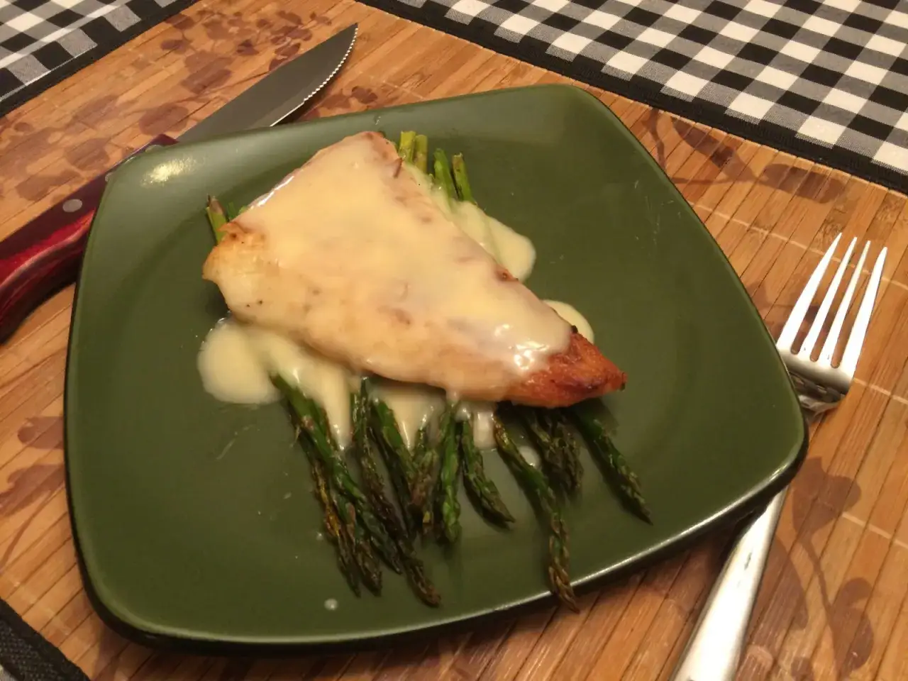 En bit fisk med kr&auml;mig beurre blanc och sparris p&aring; en gr&ouml;n tallrik. En kniv och gaffel ligger bredvid.