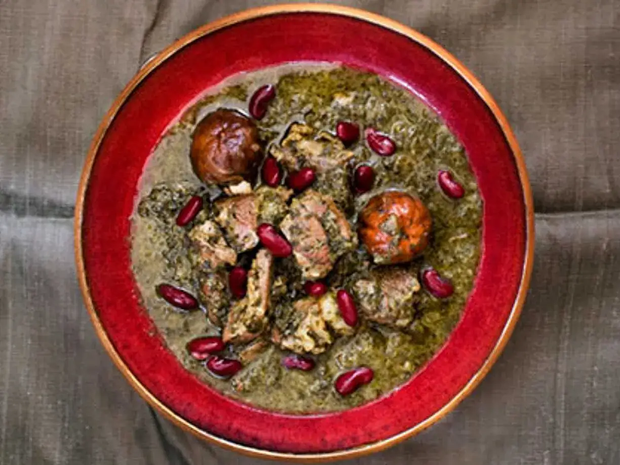 En skål med ghorme sabzi, en mustig persisk gryta med örter, kött och röda bönor, serverad i en röd kantad skål.