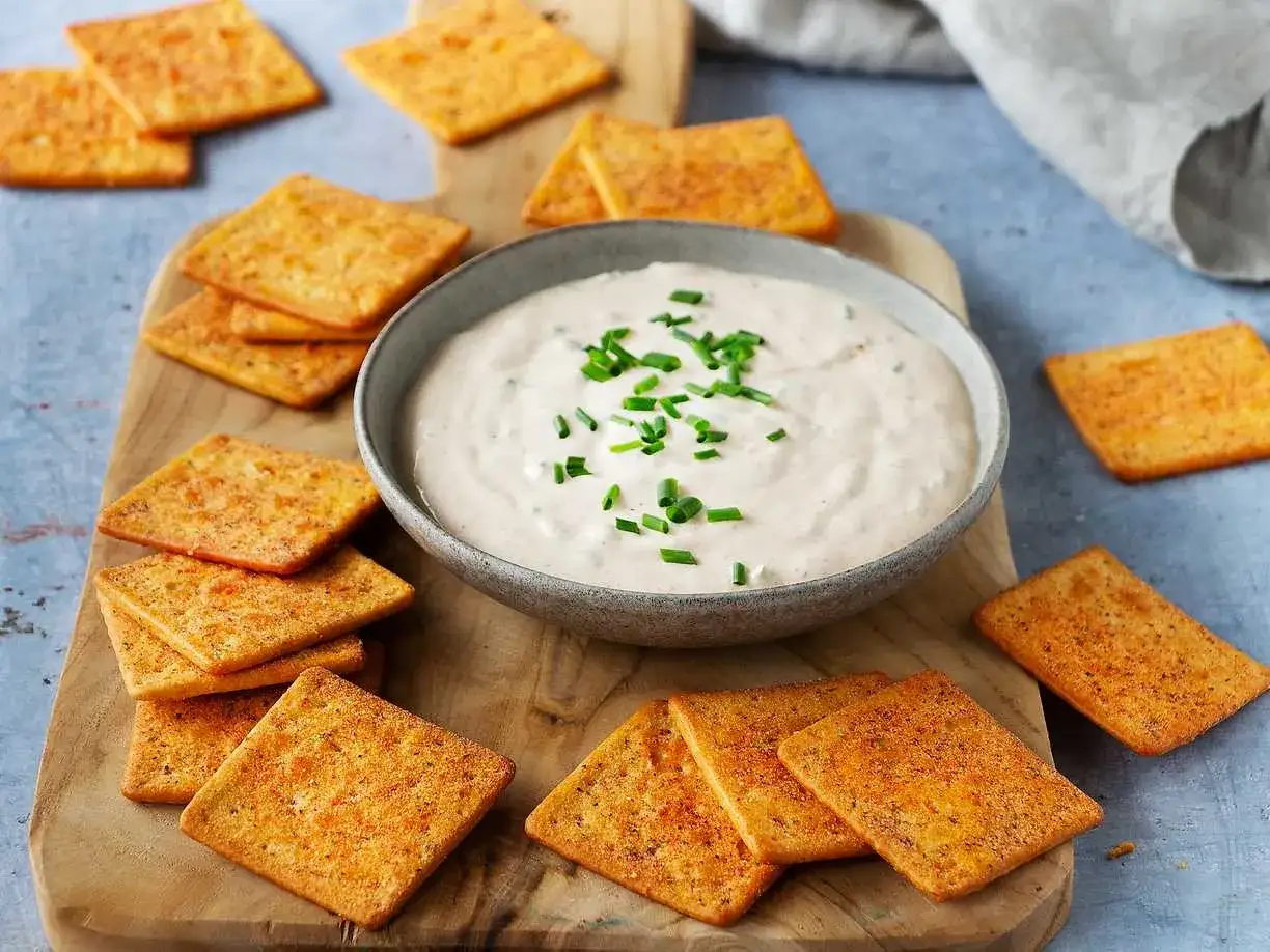 En sk&aring;l med kr&auml;mig ranch dipp, toppad med gr&auml;sl&ouml;k, omgiven av krispiga kex p&aring; en tr&auml;sk&auml;rbr&auml;da. Perfekt f&ouml;r en mysig kv&auml;ll.