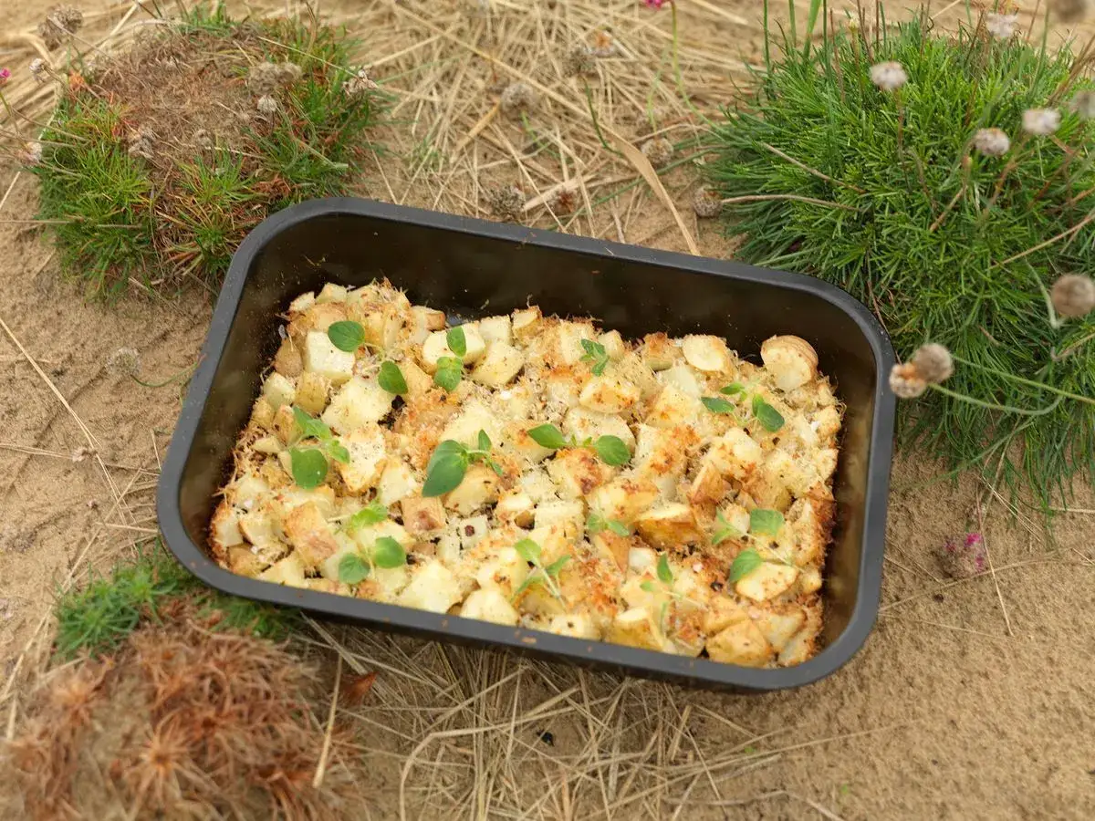 En ugnsform med gyllene, ugnsrostade smashed potatis, toppad med färska örter. Perfekt för en picknick i det gröna.