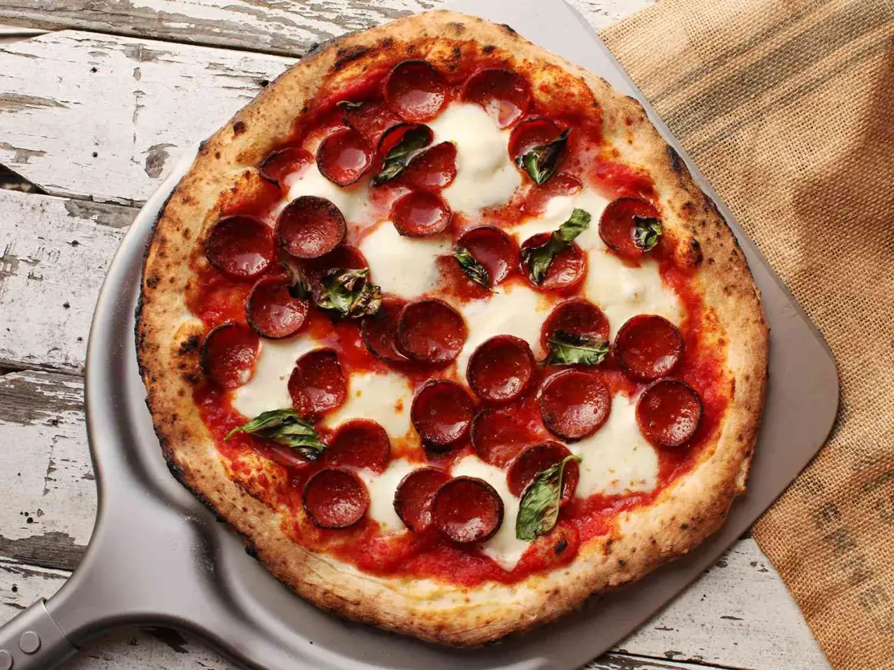En perfekt napolitansk pizza med pepperoni och basilika, redo att serveras på en pizzaspade.