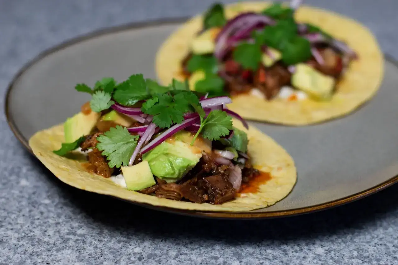 Två läckra tacos med carnitas recept, fyllda med mört kött, krämig avokado, rödlök och färsk koriander.