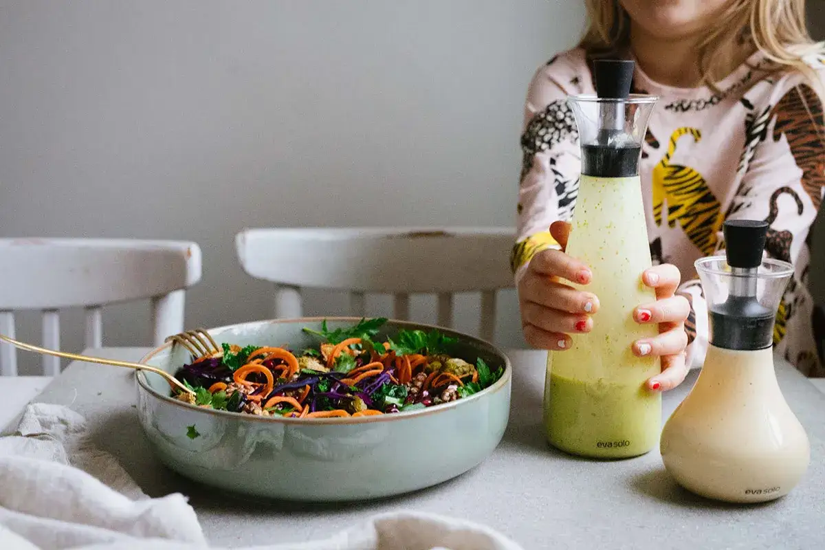 En f&auml;rgstark sallad med morotsstrimlor och r&ouml;dk&aring;l i en sk&aring;l. Bredvid st&aring;r tv&aring; flaskor med hemlagad salladsdressing, perfekt f&ouml;r ett enkelt salladsdressing recept.
