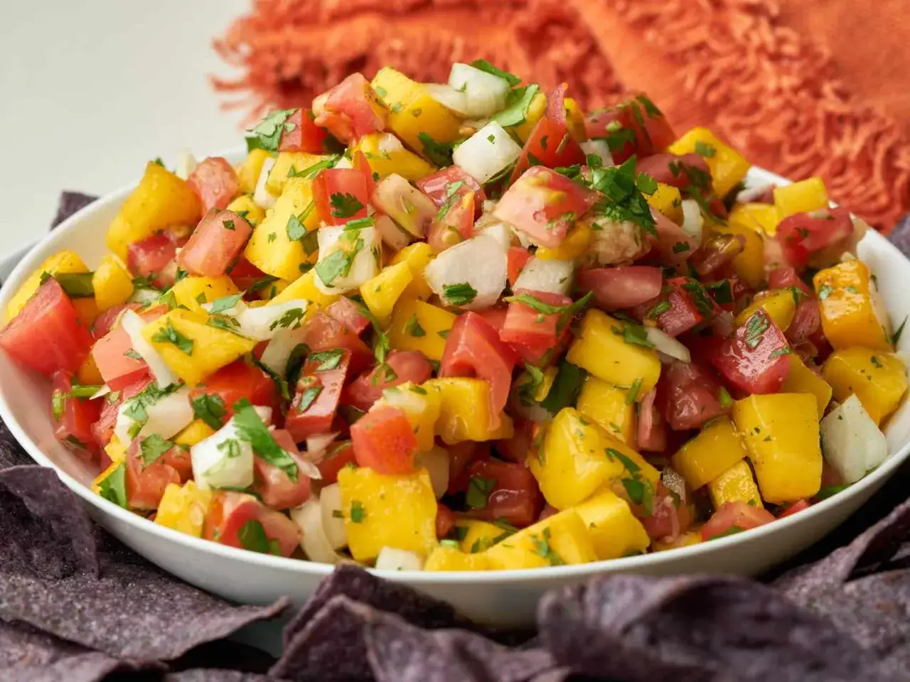En skål med färgglad mango salsa, full av tärnad mango, tomat, lök och koriander, serverad med tortillachips.