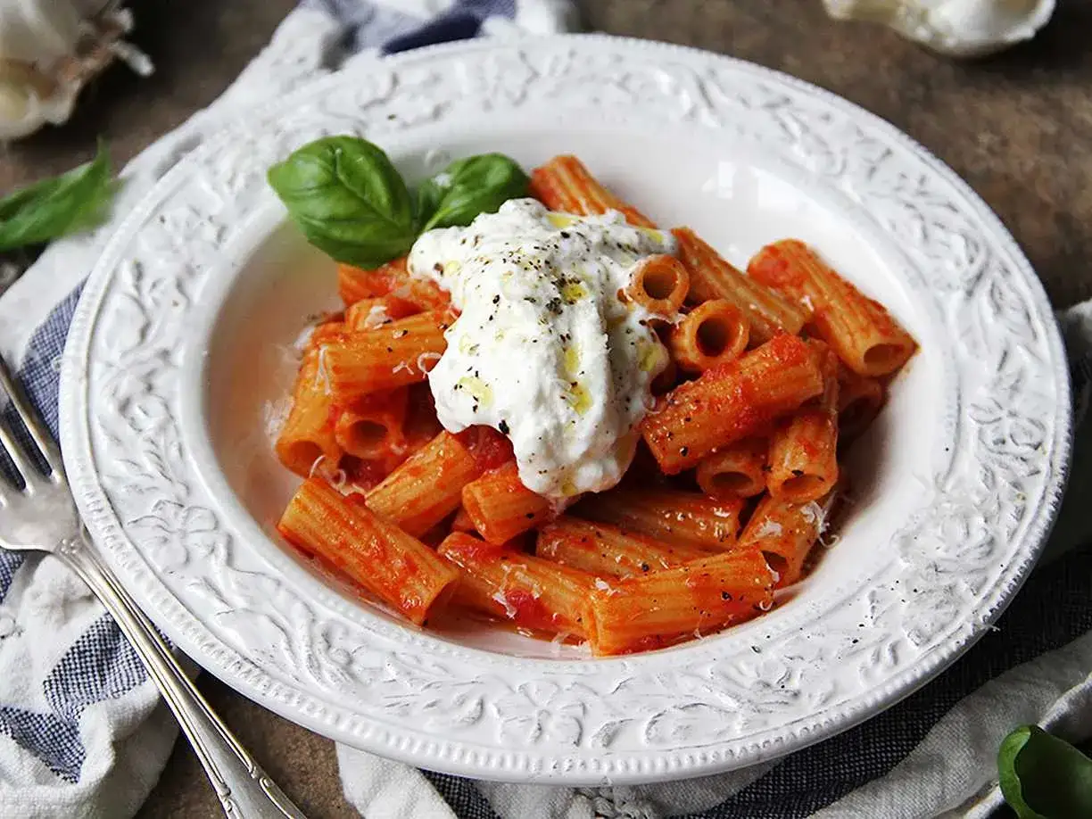 En krämig burrata pasta med rigatoni i tomatsås, toppad med färsk basilika och svartpeppar.