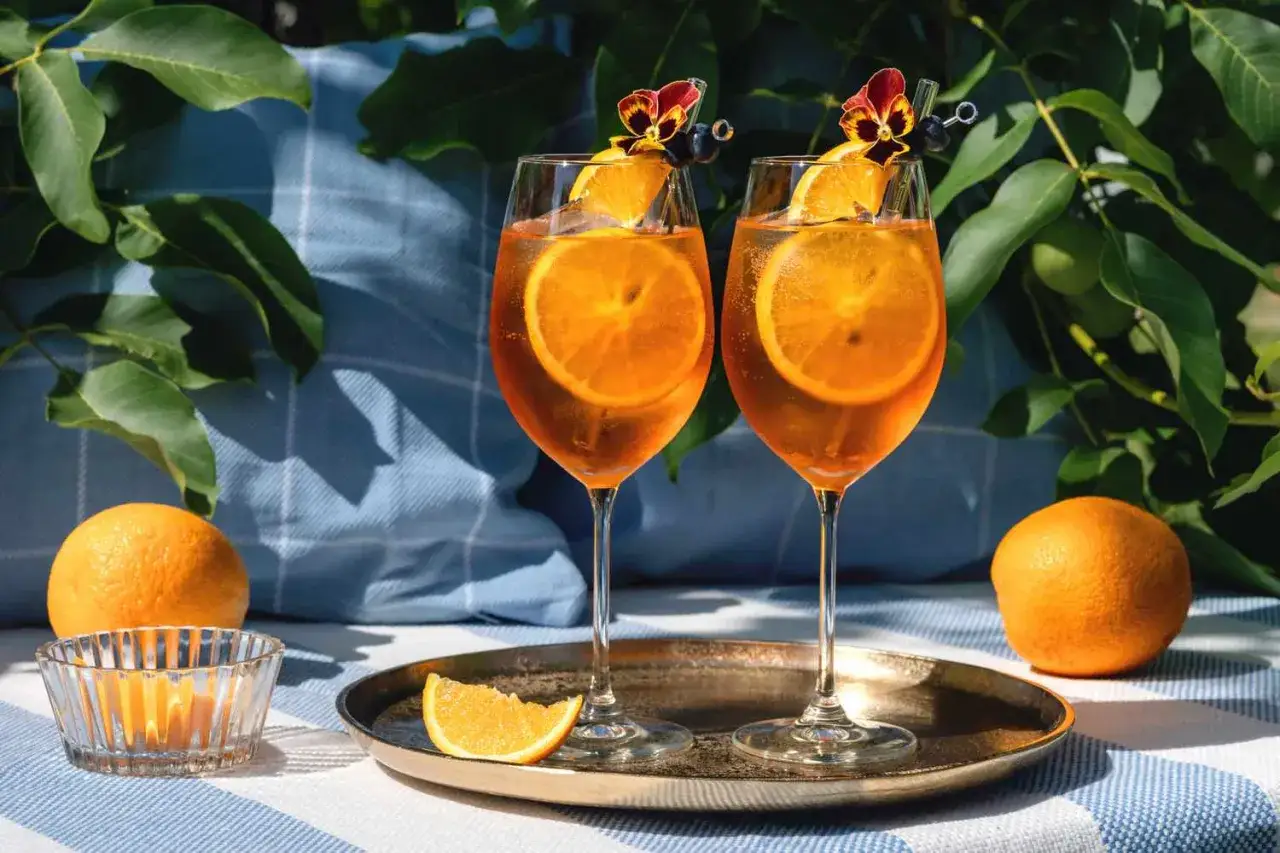Tv&aring; glas med cava aperol, garnerade med apelsinskivor och blommor, st&aring;r p&aring; ett fat.