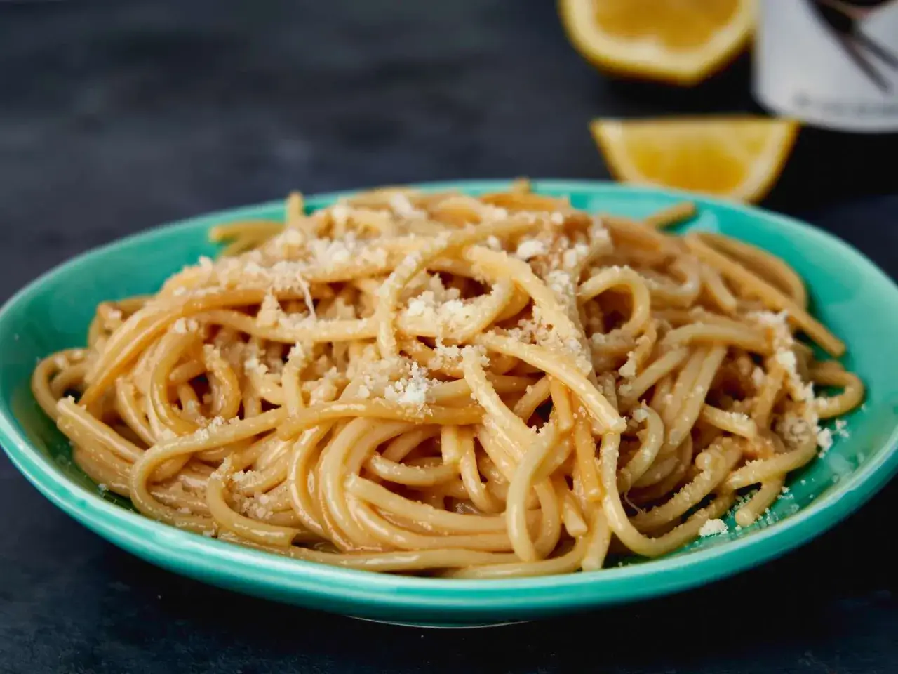 En tallrik krämig pasta limone, toppad med riven parmesan. Citronklyftor i bakgrunden.