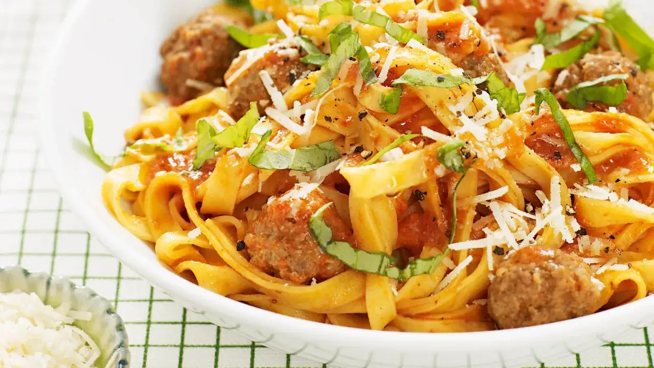 En skål med pasta och saftiga frikadeller i tomatsås, toppad med riven parmesan och färsk basilika. En klassisk och smakrik rätt.