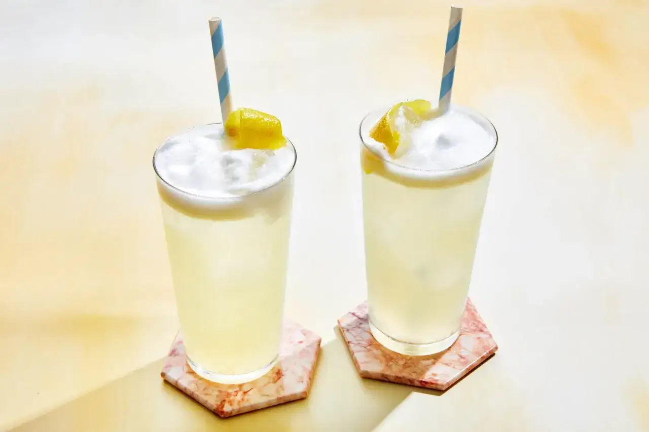 Två uppfriskande drinkar, som en Clover Club, med citronskiva och randiga sugrör.