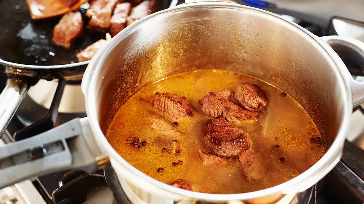 Kastrull med pulled beef i en gyllene buljong. Köttet ser mört ut och redo att serveras.