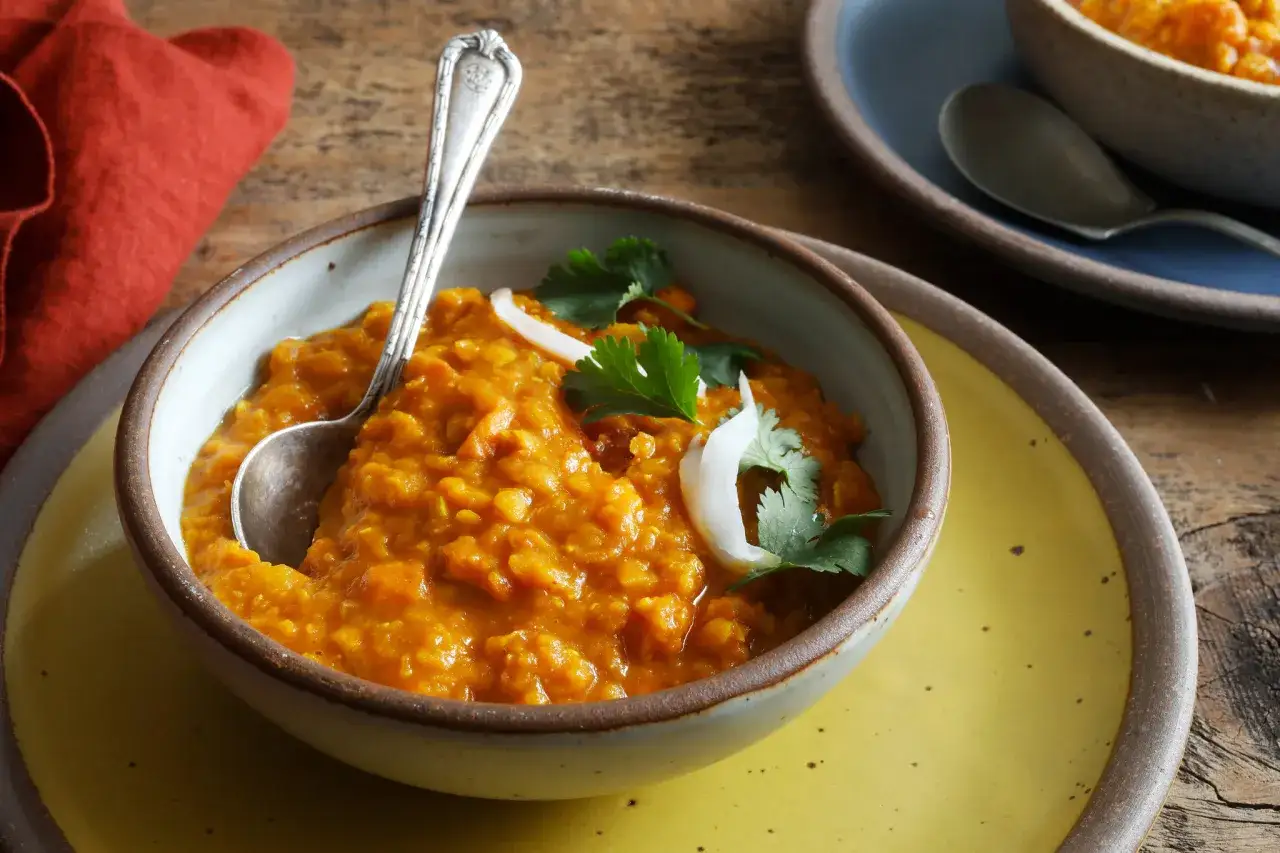En skål med varm, orange daal, garnerad med koriander och lök. Perfekt för ett mysigt daal recept.