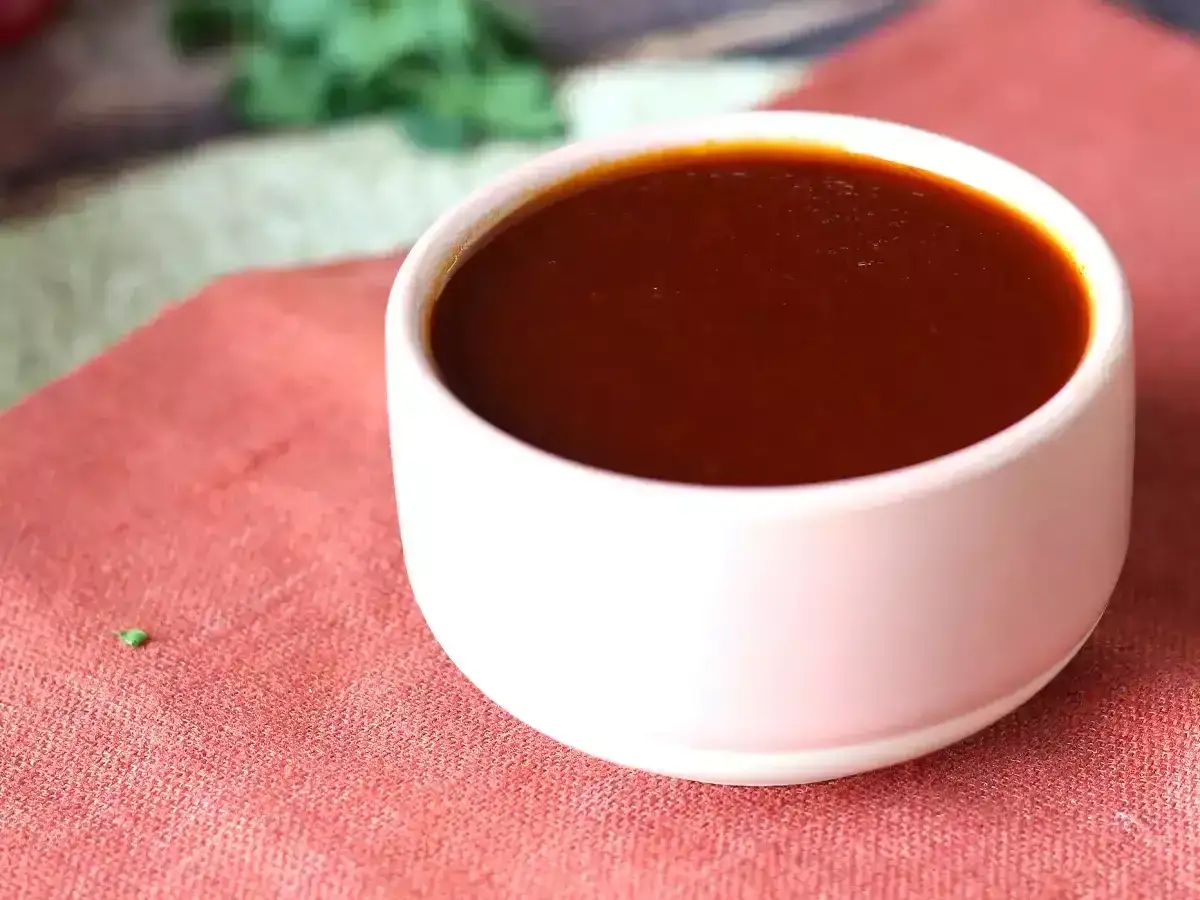 En skål med mörk, glansig bbq sås står på en röd duk. Perfekt för grillkvällen!