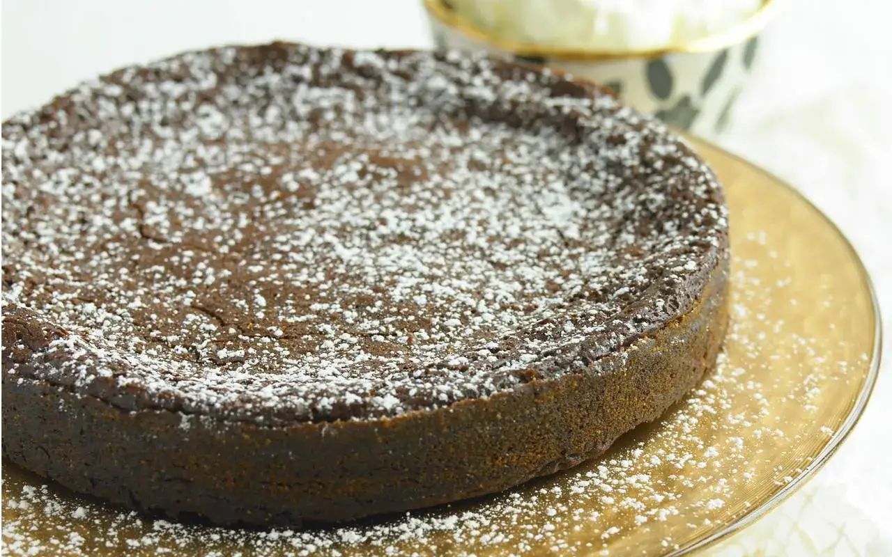 En mörk chokladkaka, pudrad med florsocker, ligger på ett guldfärgat fat. Den ser ut som en perfekt lava cake.