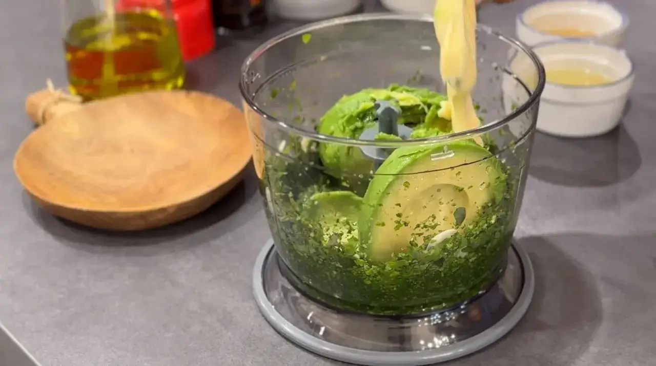 Avokado och örter i en mixer för ett krämigt green goddess dressing recept.