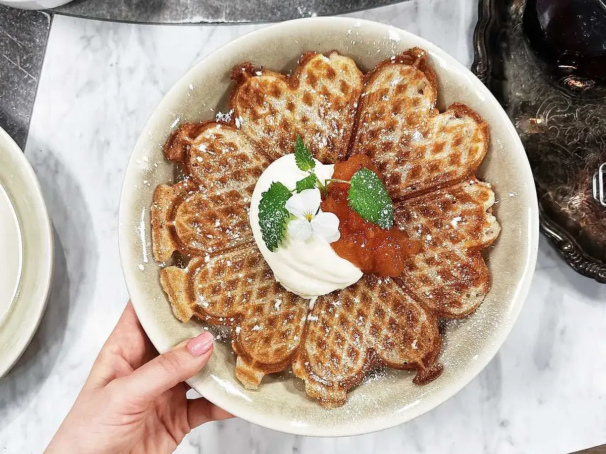 En vacker tallrik med glutenfria våfflor formade som ett hjärta, toppade med vispgrädde, sylt och en blomma.