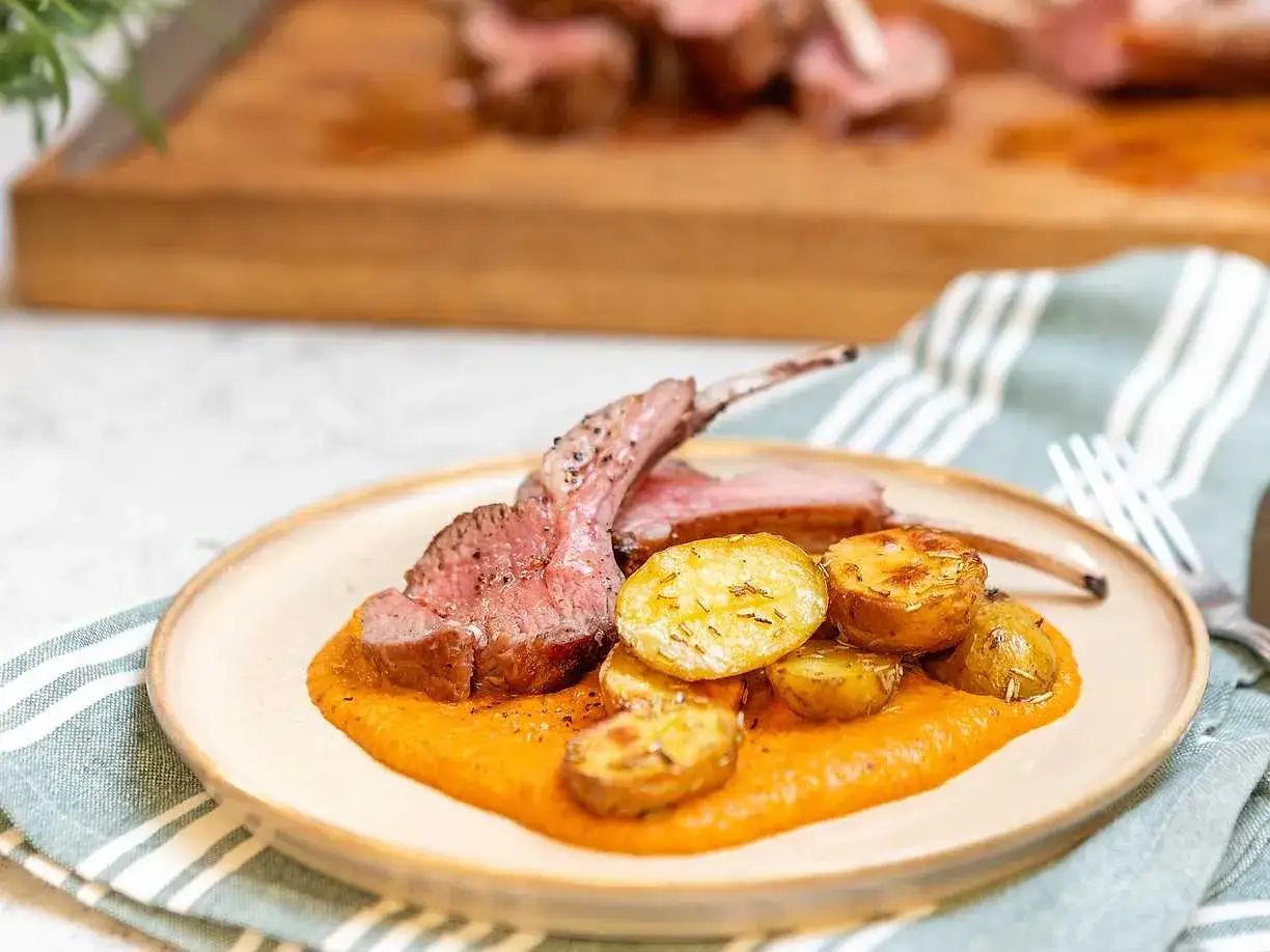 En tallrik med lammracks, rostade potatisar och en krämig sås. Ett perfekt lammracks recept för en festmåltid.