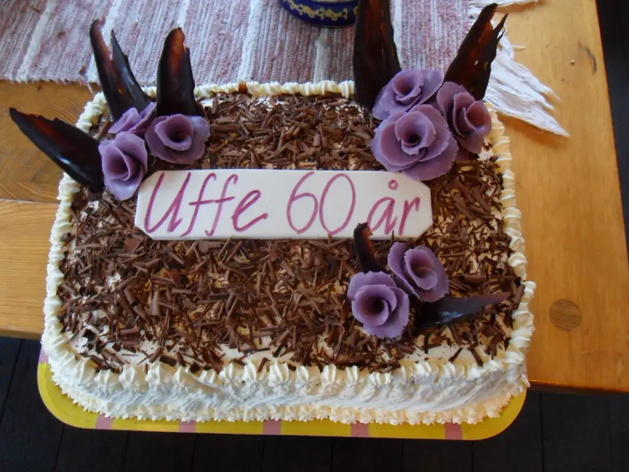 En stor t&aring;rtbotten i l&aring;ngpanna, dekorerad med chokladsp&aring;n, gr&auml;dde och lila blommor. Grattis till Uffe 60 &aring;r!